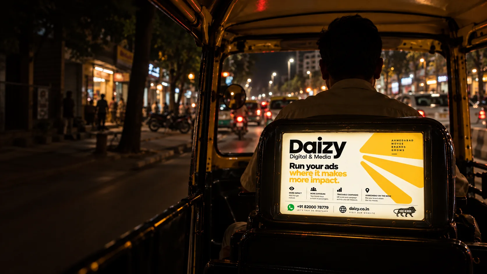 A lit advertising board fixed behind the driver's seat of an auto-rickshaw, photographed at night on an Ahmedabad street.